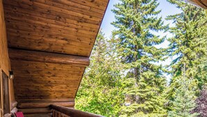 A wooden deck with a railing, a red chair, and a view of trees. - Mike Wiegele Helicopter Skiing (Blue River)