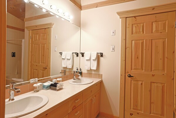 A bathroom with two sinks, a large mirror, wooden doors, and a towel rack. - Mike Wiegele Helicopter Skiing (Blue River)