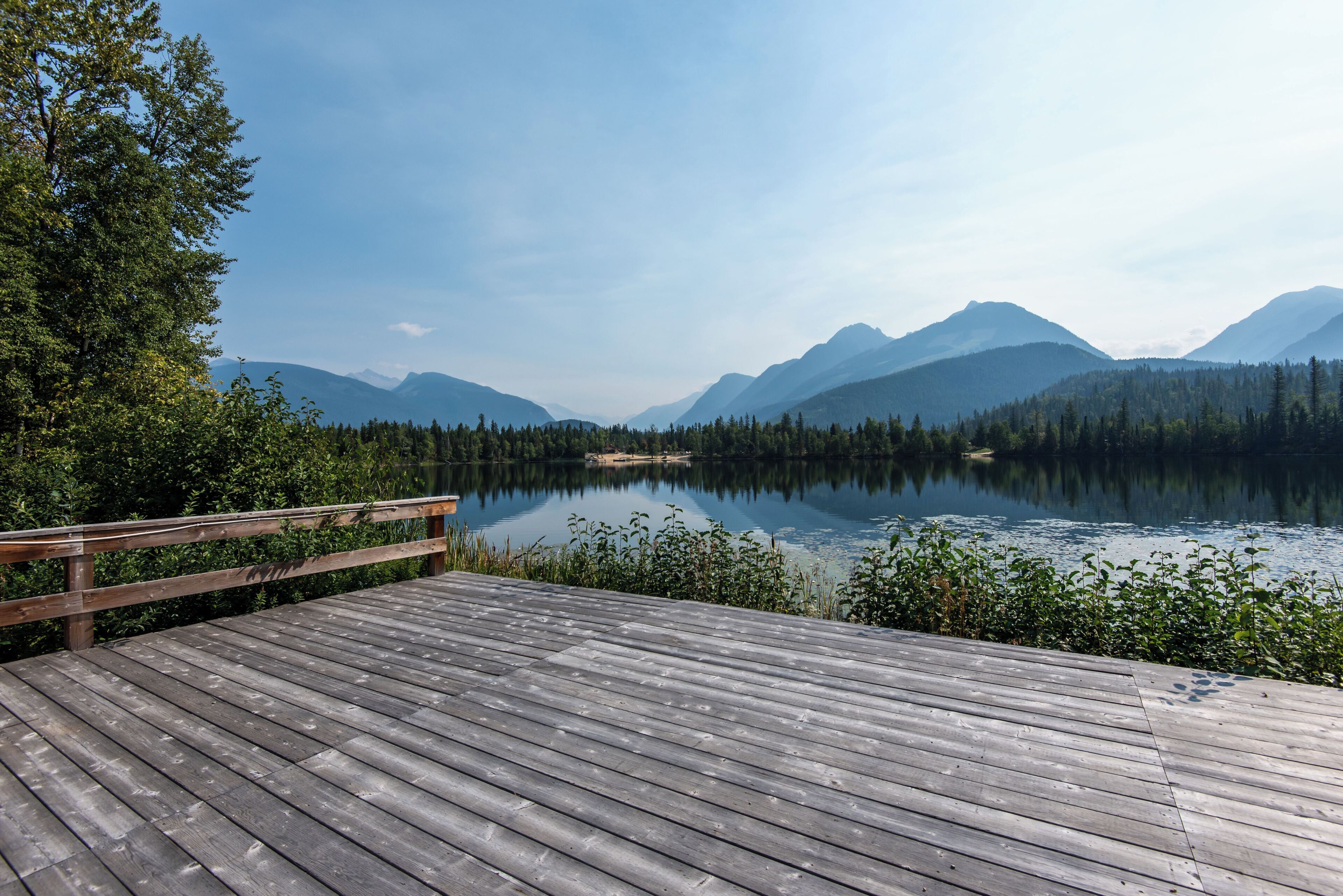 A wooden deck overlooking a calm lake with mountains in the background.