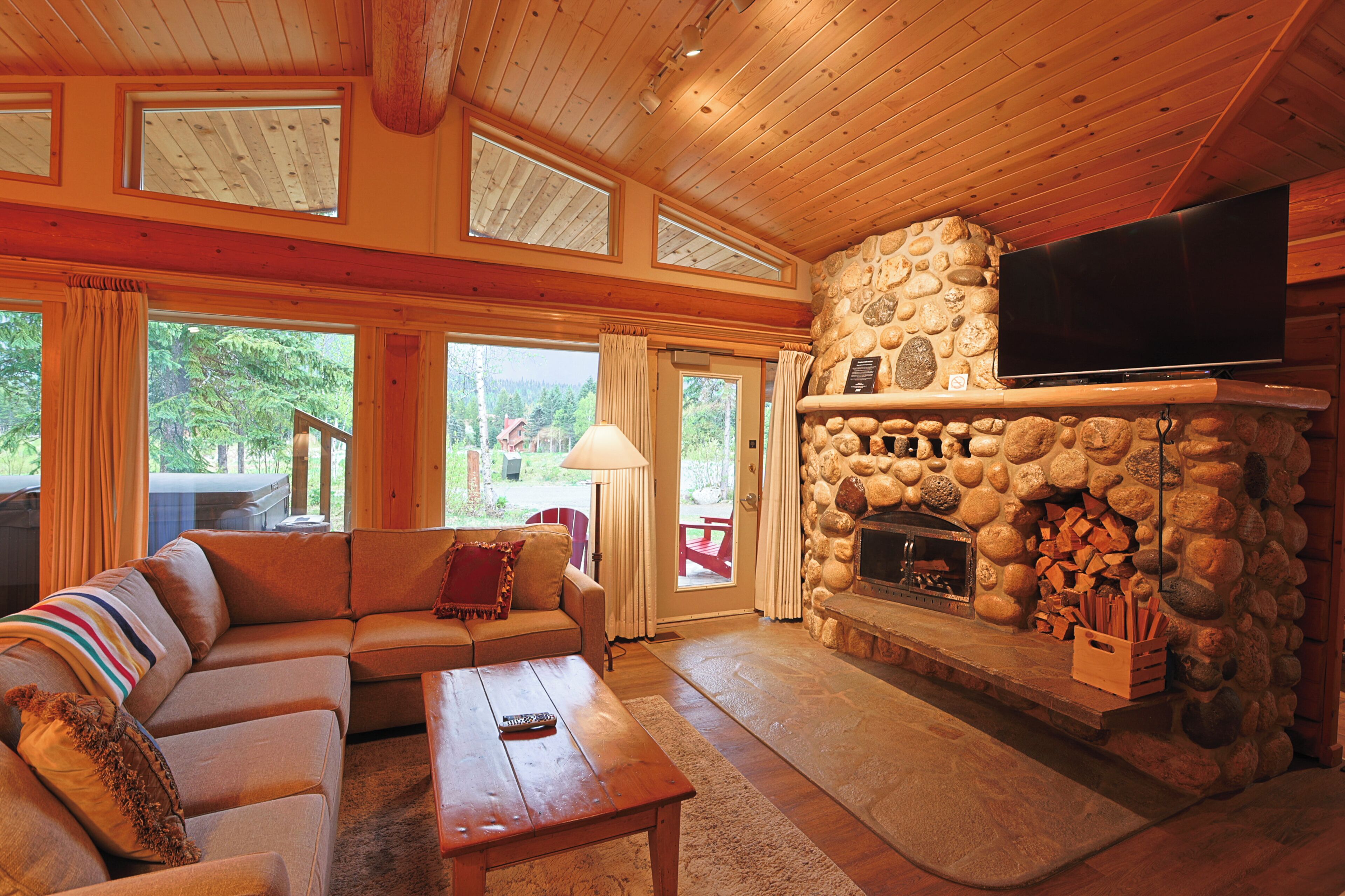 A cozy living room with a stone fireplace, a flat-screen TV mounted above it, a comfortable sofa, and a wooden coffee table.
