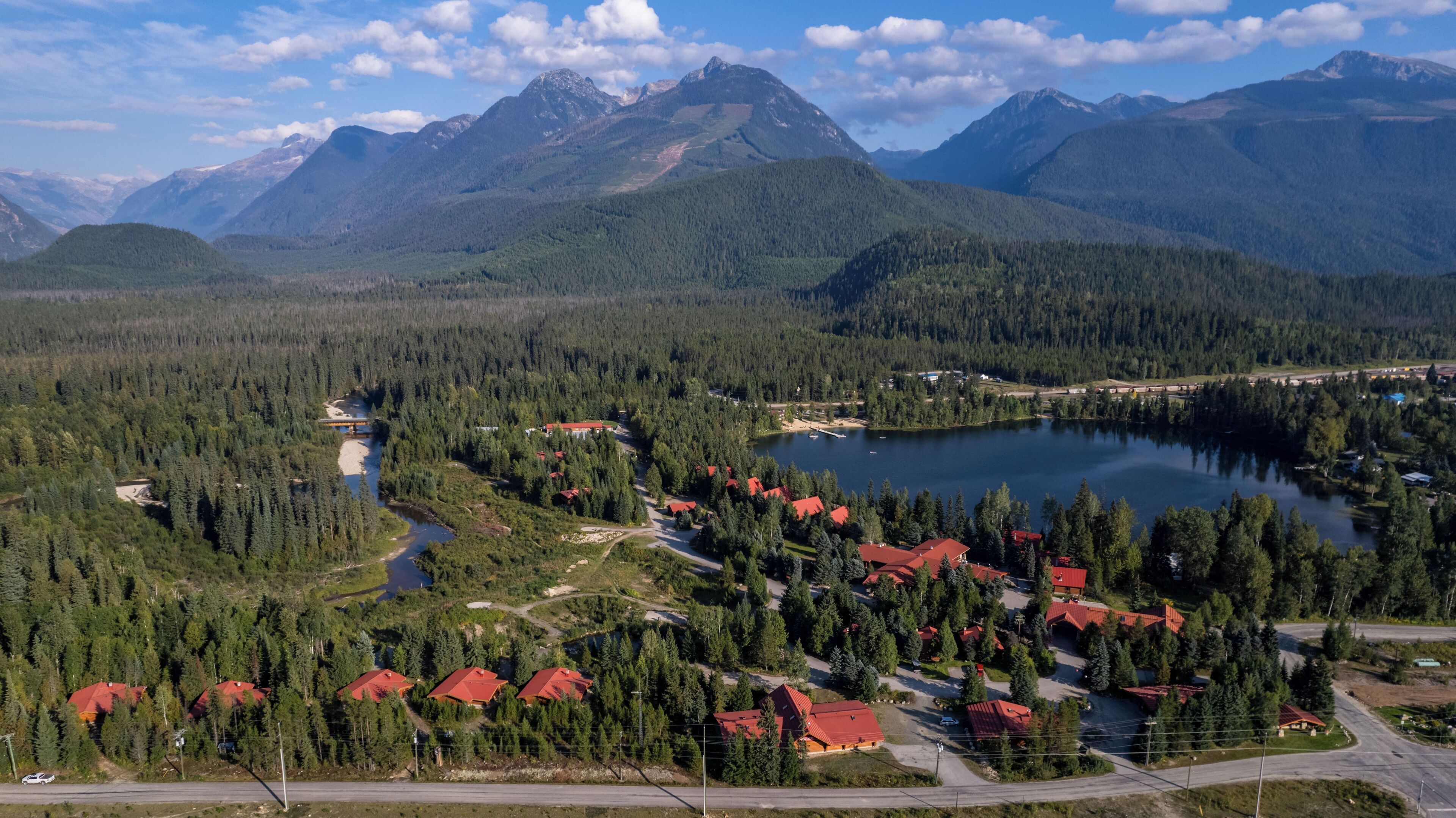 Un paysage montagneux avec un lac, entouré de forêts denses et de bâtiments aux toits rouges, probablement un lieu de villégiature ou une zone touristique.