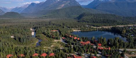 Un paysage montagneux avec un lac, entouré de forêts denses et de bâtiments aux toits rouges, probablement un lieu de villégiature ou une zone touristique.