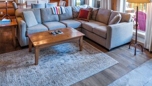 A cozy cabin interior with a sectional sofa, wooden ceiling, and large windows. - Mike Wiegele Helicopter Skiing (Blue River)