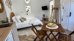 A modern bedroom with a bed, bedside tables, a TV, and a wooden dining table with chairs. - Cocon Cosy & Chaleureux à Pézenas: Chez Roméo (Pézenas)
