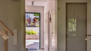 A hallway with a door leading to a balcony with plants and a view of a building.