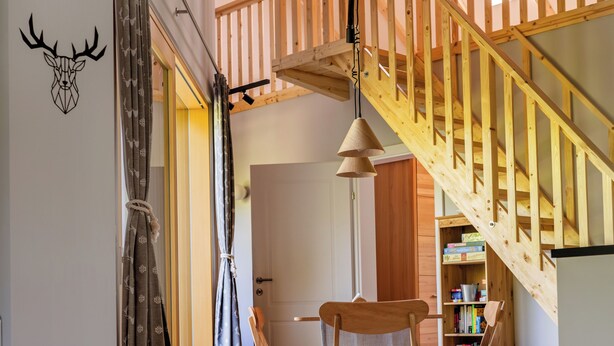 A room with a wooden staircase, a ceiling fan, a wooden chair, and a table with a floral tablecloth.