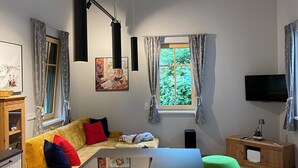A modern living room with a high ceiling, a large window, a sofa, a dining table, and a TV.