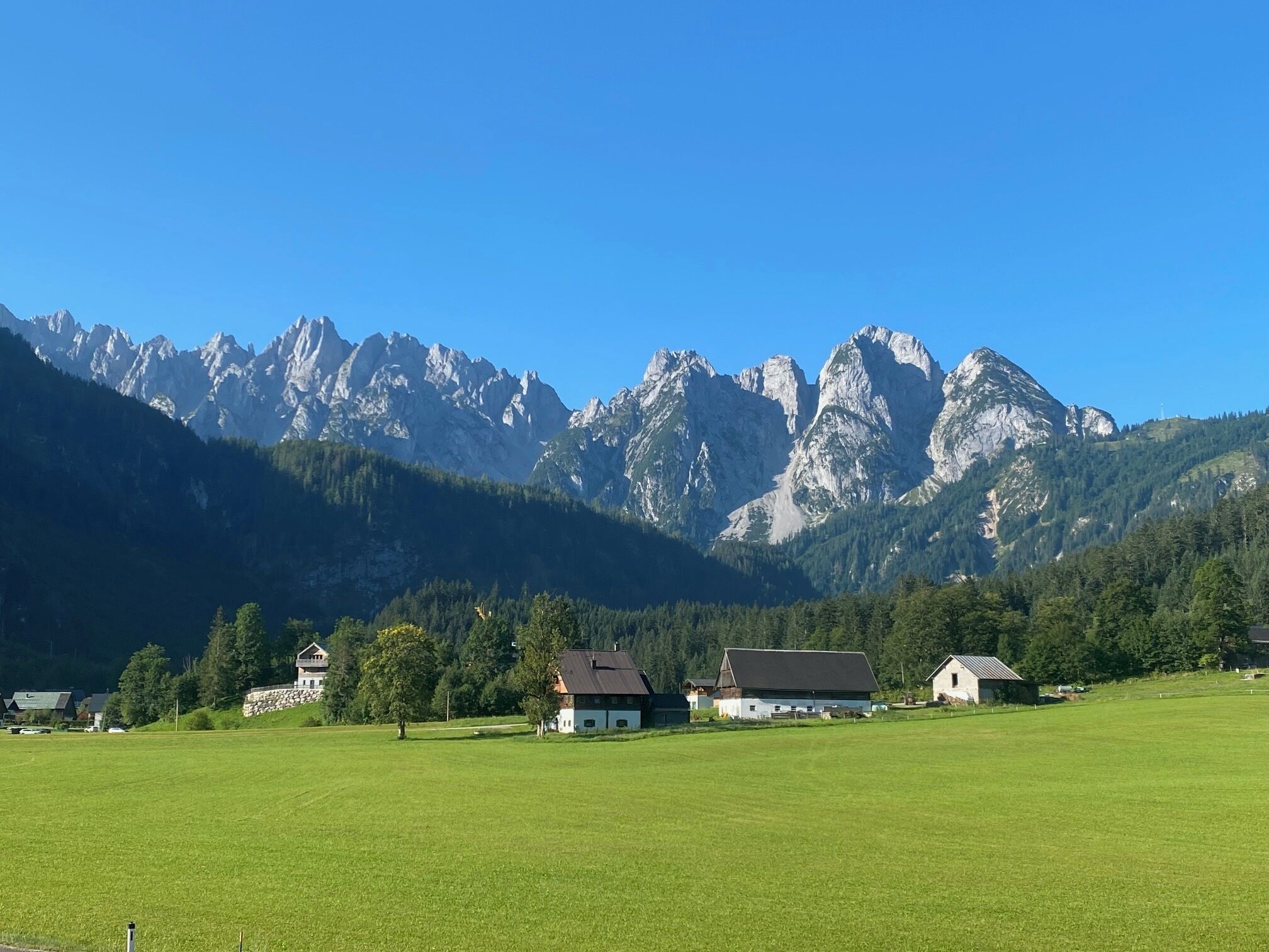 Paisaje rural con un campo, una casa de campo y una cadena montañosa al fondo.