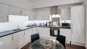 Una cocina moderna con armarios blancos, una mesa de comedor de vidrio y electrodomésticos de acero inoxidable.