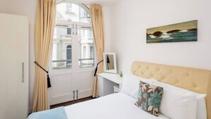 Habitación de hotel con una cama, una ventana con cortinas, un cuadro en la pared y vistas a edificios.