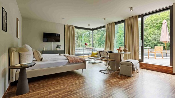 A modern hotel room with a large bed, a desk, and a view of the outdoors.