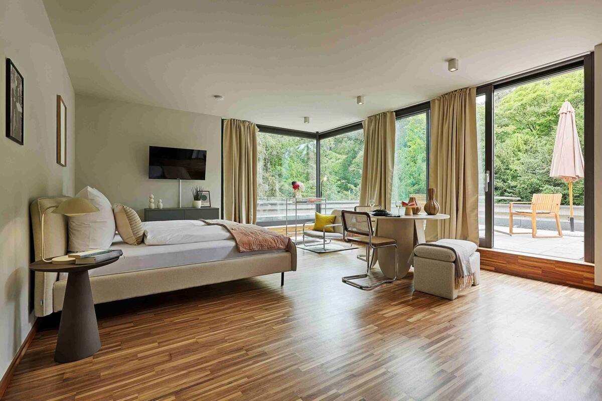 A modern hotel room with a large bed, a desk, and a view of the outdoors.