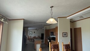 Un comedor amplio con una mesa y sillas de madera, una cocina al fondo y un ventilador de techo.