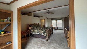 Un dormitorio con una cama, una estantería de madera, un ventilador de techo y una ventana con persianas.