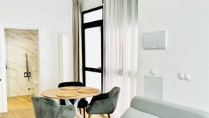 A modern living room with a grey sofa, a round table with two chairs, and a large window with curtains. - A (VA070.2.4) TH Mediterranean Suites 4 (Valencia / València)