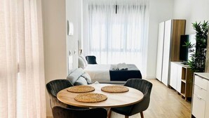 A modern hotel room with a bed, a dining area with a table and chairs, a TV, and a plant. - A (VA070.2.4) TH Mediterranean Suites 4 (Valencia / València)