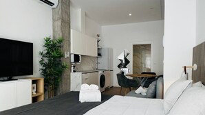 A modern hotel room with a large bed, a flat-screen TV, a small kitchenette, and a dining area. - A (VA070.2.4) TH Mediterranean Suites 4 (Valencia / València)