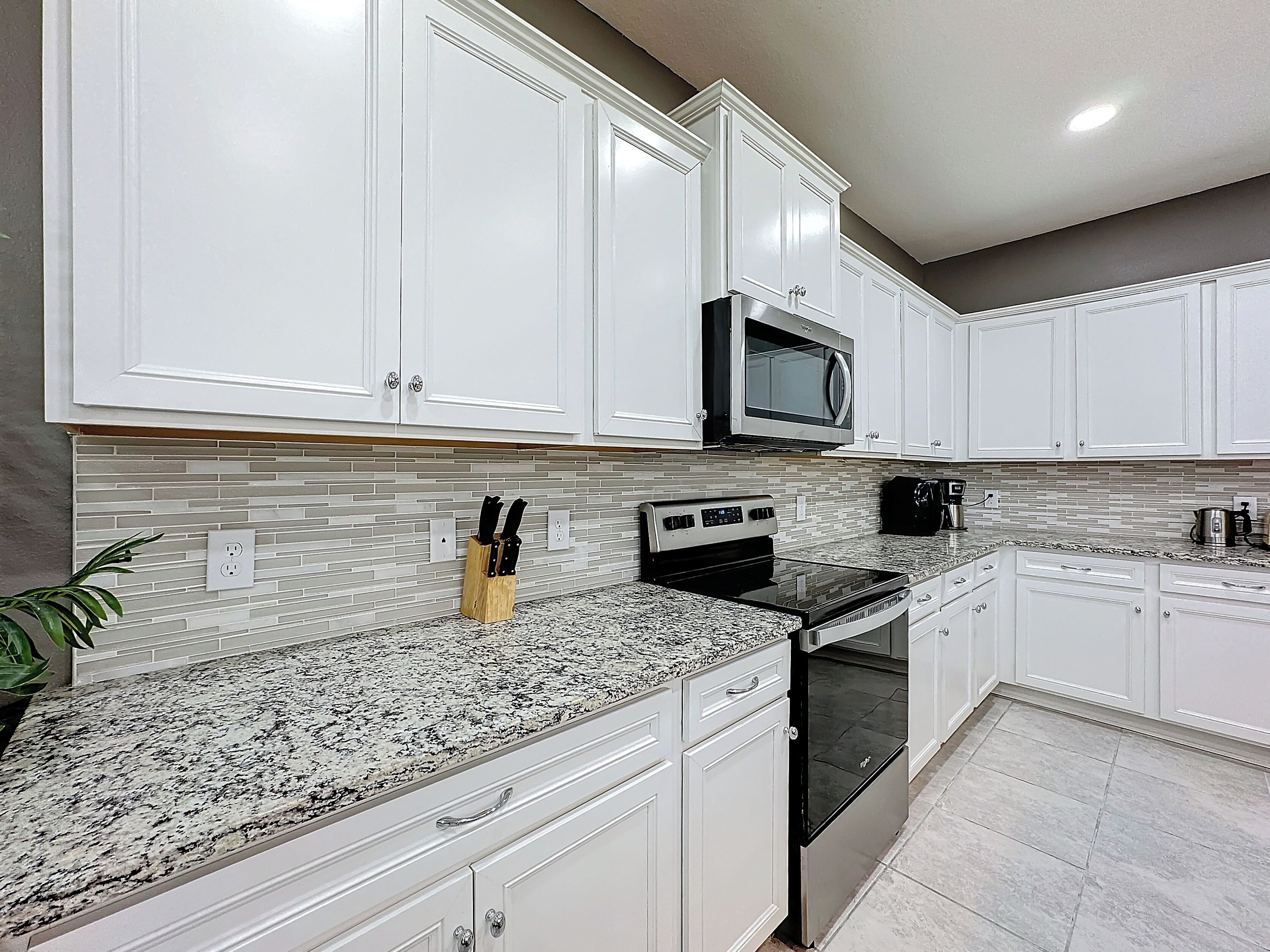 A modern kitchen with white cabinets, a granite countertop, a built-in microwave, and a dishwasher.