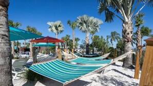 Eine Hängemattenlounge mit gestreifter Liegefläche, Palmen und blauem Himmel.