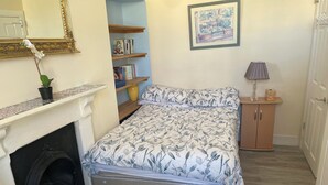 A bedroom with a bed, a small cabinet, a bookshelf, a mirror, and a fireplace.
