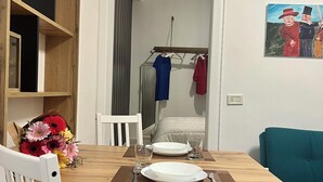 A dining area with a wooden table, white chairs, and a red cushion. There is a bouquet of flowers on the table, and a painting on the wall. - Ludo’s Flat Bari Center  (Bari)