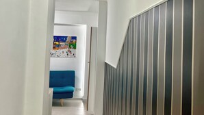A hallway with a blue sofa, a colorful abstract painting, and a striped wall. - Ludo’s Flat Bari Center  (Bari)