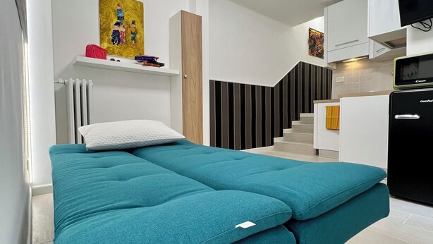 A modern, compact living space with a teal sofa bed, a small kitchen area, and a staircase leading to an upper level. - Ludo’s Flat Bari Center  (Bari)
