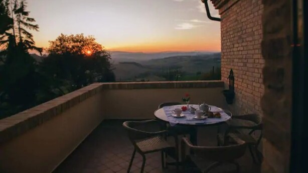 Un balcon avec une table préparée pour le thé, offrant une vue panoramique sur un paysage magnifique au coucher du soleil.