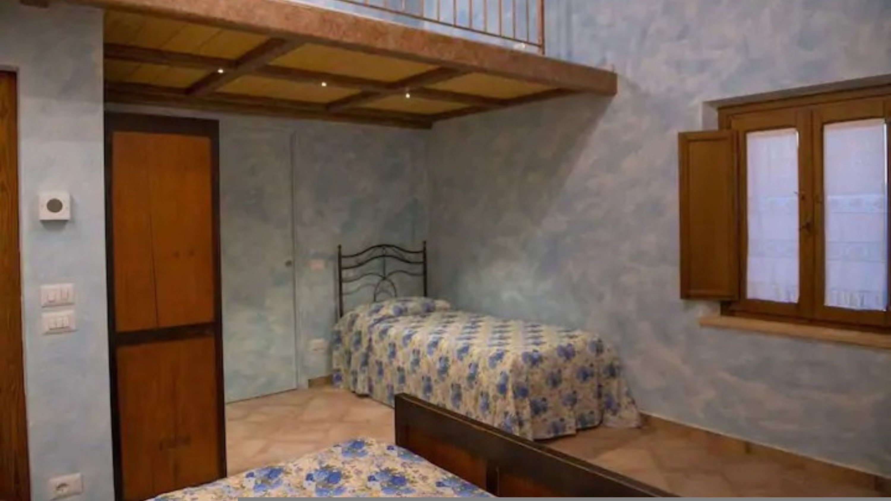 A small bedroom with a single bed, a wooden door, and a window with shutters.