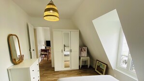 Une chambre à coucher comprenant un lit, une commode, une armoire, un luminaire suspendu et une fenêtre.