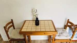 Une table à manger agrémentée d’un vase noir et de fleurs blanches, entourée de deux chaises en bois dotées d’assises rembourrées.