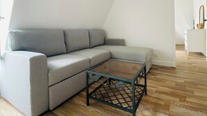Un salon moderne avec un canapé d’angle gris, une table basse en verre et un plancher en bois.