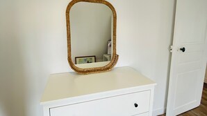 Une commode blanche avec un miroir et trois tiroirs, placée contre un mur blanc.