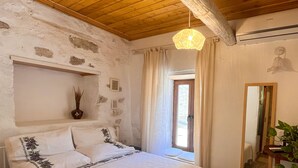 A bedroom with a wooden ceiling, a bed with white bedding, a bedside table with a vase, and a window with curtains. - Eskikent Alaçatı (Cesme)