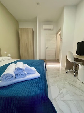 A hotel room with a bed, a desk, a chair, and an air conditioning unit.