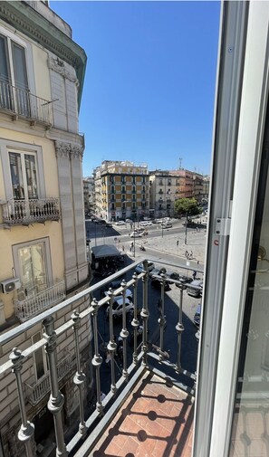 Un balcón con barandillas ornamentales que da a una calle concurrida y edificios al fondo.