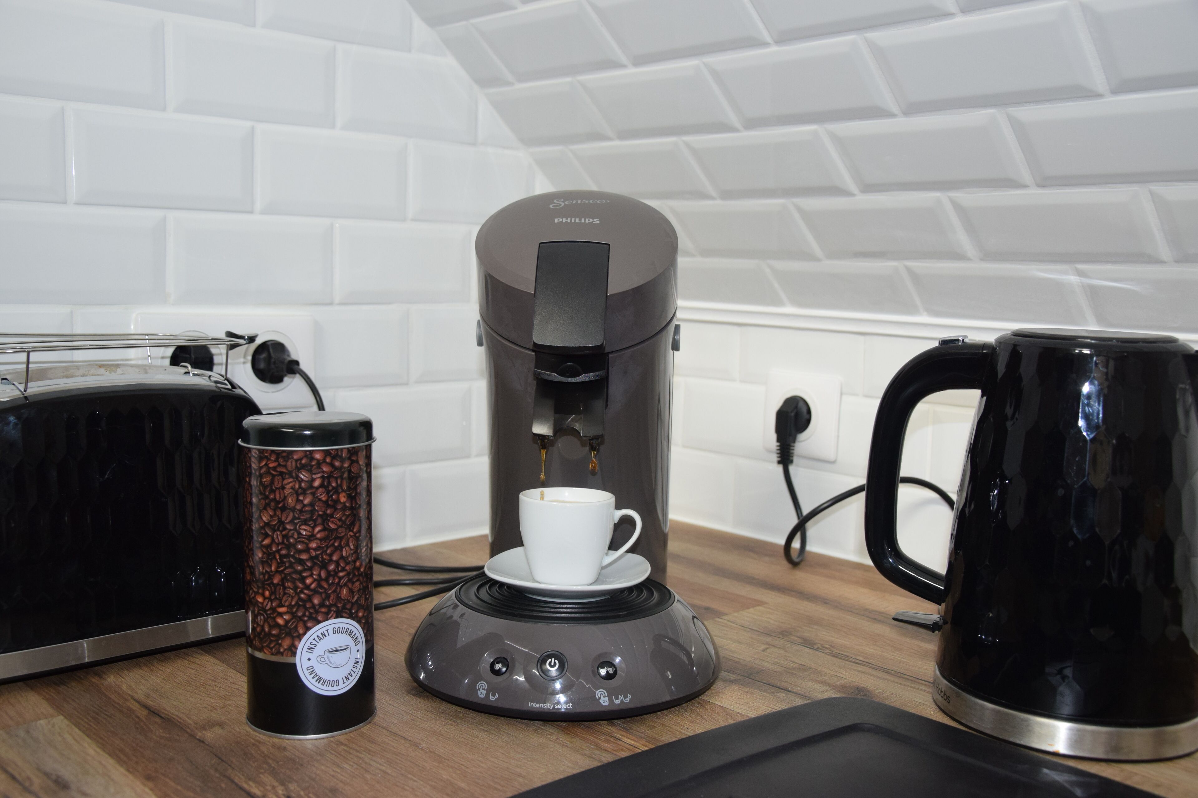 Uma cafeteira, uma chávena de café e uma chaleira sobre uma mesa de madeira.