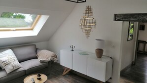A modern living room with a gray sofa, a white cabinet, a small round table, and a ceiling light fixture. - "Le Rooftop de la fontaine", in a quiet, green setting (Luisant)