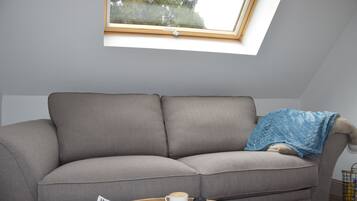 A grey sofa with a blue blanket, a coffee cup, and a magazine on a wooden coffee table.