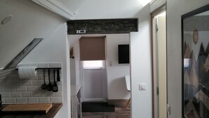 A modern kitchen with a wooden countertop, white cabinets, and a dark backsplash. A hallway leads to a bedroom with a large window and a door. - "Le Rooftop de la fontaine", in a quiet, green setting (Luisant)