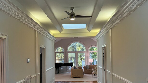 A spacious hallway with a piano, a ceiling fan, and large arched windows.