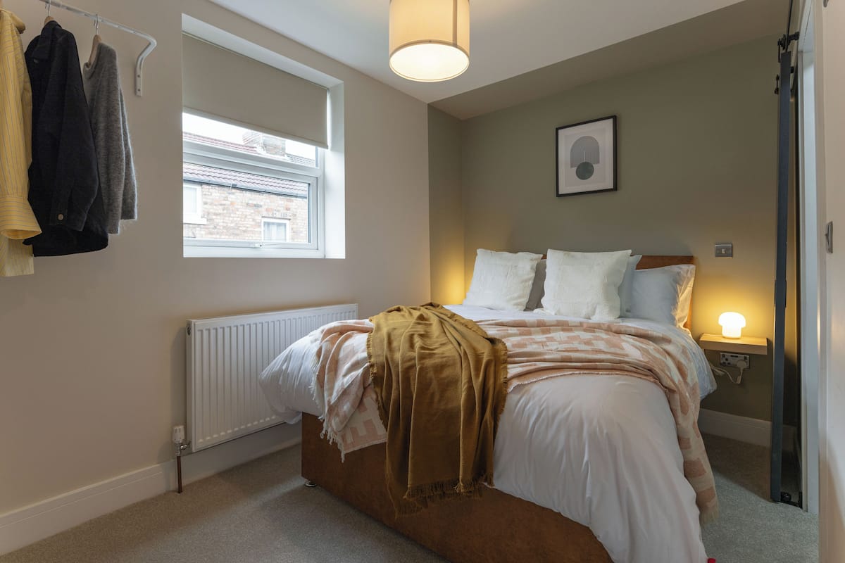 A bedroom with a bed, a window, a radiator, and a hanging clothes rack.