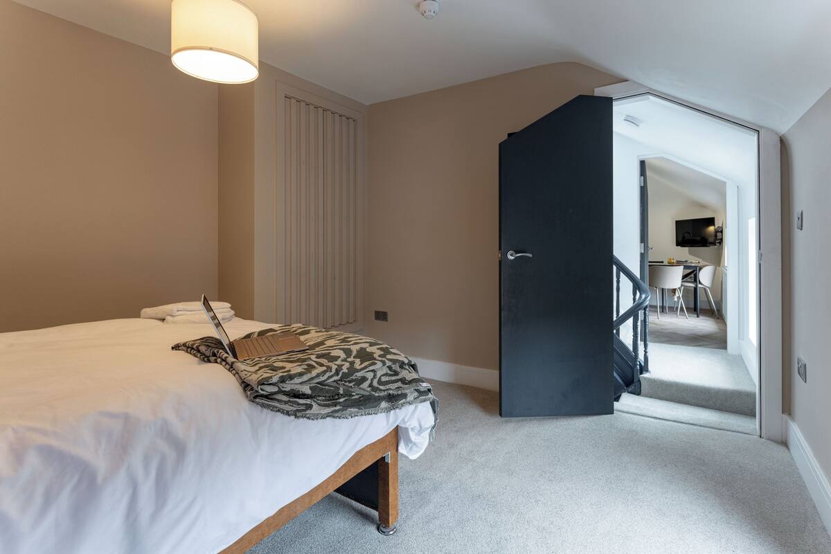 A bedroom with a bed, a laptop, and a patterned throw blanket.