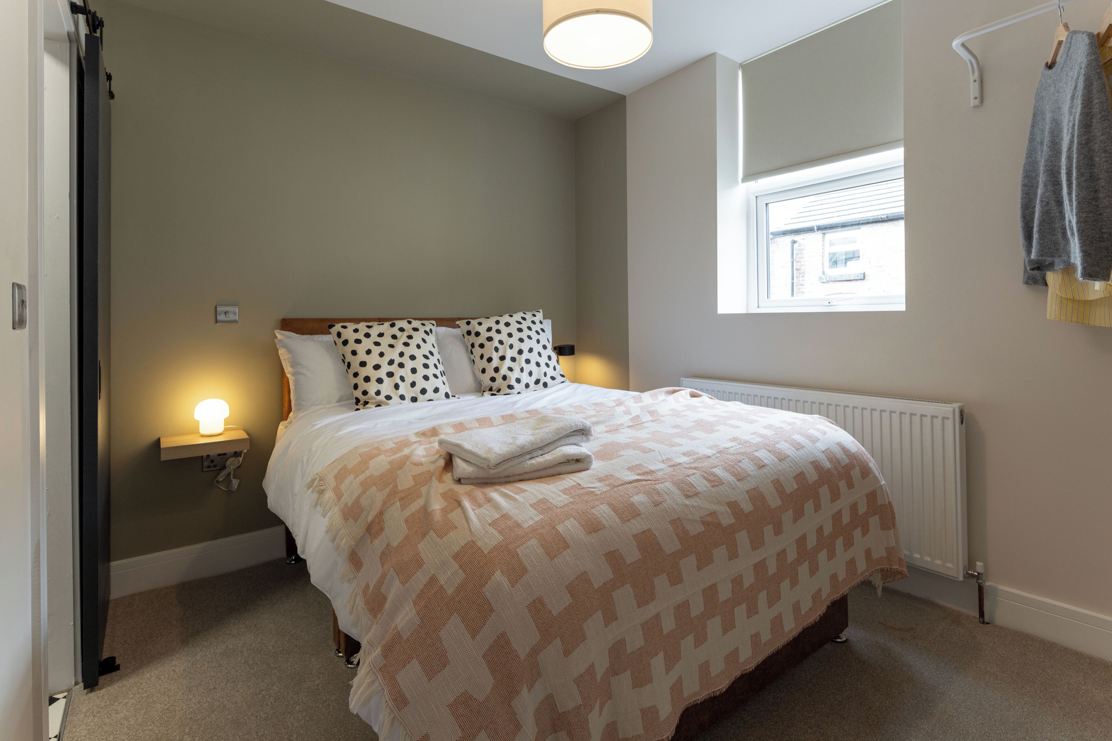 A bedroom with a bed, a bedside lamp, a window, and a radiator.
