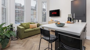 A modern kitchen with a large island, a green sofa, and a flat-screen TV mounted on the wall. - Broughton Place (Liverpool)
