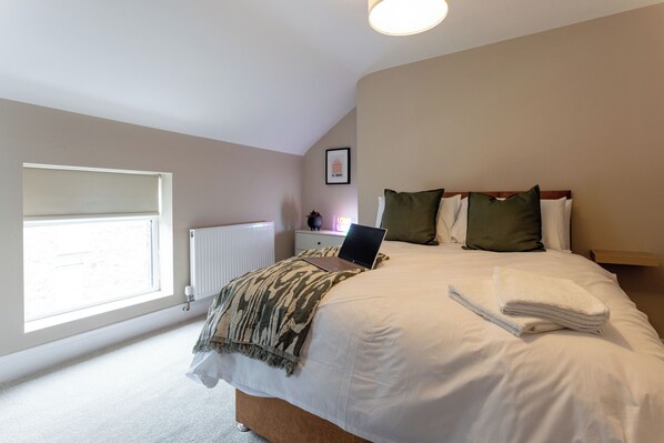 A bedroom with a bed, a laptop, a radiator, a window, and a framed picture on the wall. - Broughton Place (Liverpool)