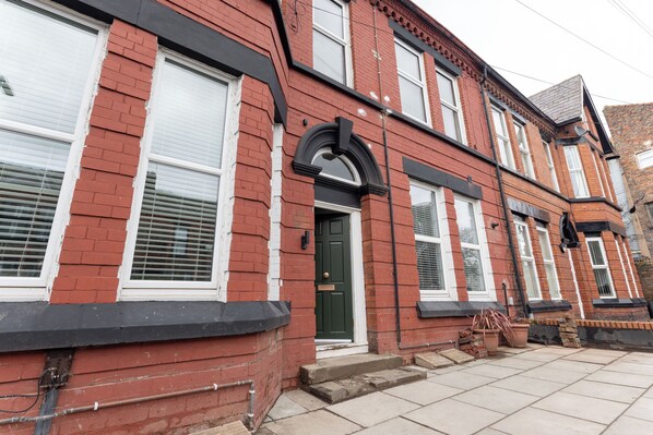A red brick terraced house with a green door, white windows, and a black front step. - Broughton Place (Liverpool)
