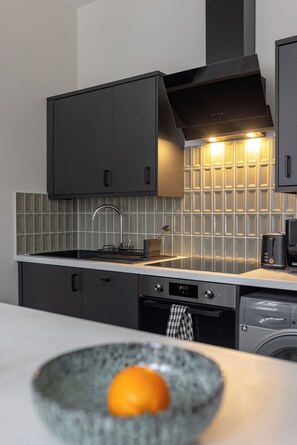A modern kitchen with dark cabinetry, a tiled backsplash, and a dishwasher. - Broughton Place (Liverpool)