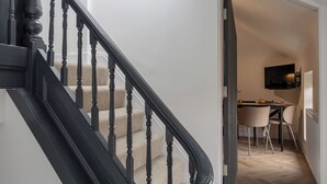 A staircase with a black handrail leading to a room with a desk, chair, and a mounted television. - Broughton Place (Liverpool)
