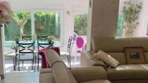 A living room with a beige sofa, a dining table with chairs, and a view of the outdoors through large windows. - La Villa Provençale (Mougins)